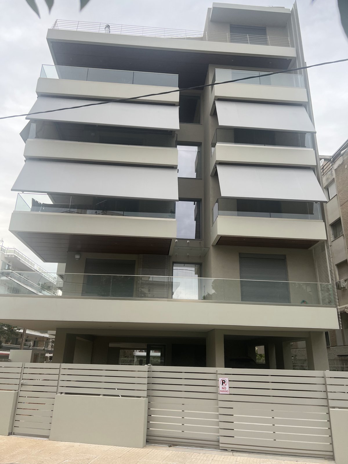 Γκρι κασετίνες τέντες σε μοντέρνα πολυκατοικία με γυάλινα κάγκελα, εγκατάσταση Pergotenta